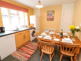A kitchen with wooden cabinets a dining table set with plates glasses and cutlery a refrigerator washing machine and a colorful rug at Maiden Moor in Grange near Keswick