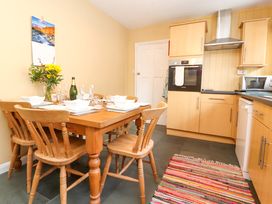 A kitchen with a wooden dining table set for six people wooden chairs kitchen cabinets and a colorful rug Maiden Moor Grange near Keswick