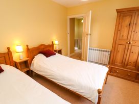 A bedroom with two single beds bedside tables with lamps a wooden wardrobe and an open door at Maiden Moor in Grange near Keswick