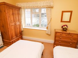 A bedroom with two single beds a wooden wardrobe a wooden chest of drawers with a flower vase a window with curtains and a wall mirror at Maiden Moor in Grange near Keswick