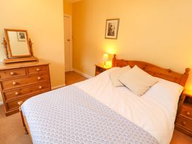 A bedroom with a wooden bed frame two pillows a bedside table with a lamp a wooden dresser with a mirror and a framed picture on the wall at Maiden Moor Grange near Keswick