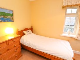 A bedroom with a single wooden bed and white bedding a wooden dresser with a lamp a window with curtains and a vase on the windowsill at Maiden Moor in Grange near Keswick