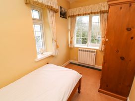 A small bedroom with a single bed a wooden wardrobe and two windows with curtains at Maiden Moor in Grange near Keswick