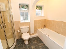 A bathroom with a shower, toilet, bathtub, and two windows at Maiden Moor in Grange near Keswick
