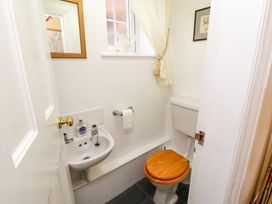 A small bathroom with a sink hand soap mirror toilet with wooden seat roll of toilet paper and a window with cream curtain at Maiden Moor in Grange near Keswick