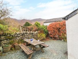 An outdoor seating area with a wooden picnic table set on gravel near a stone wall and plants at Maiden Moor in Grange near Keswick