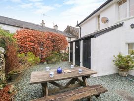 An outdoor courtyard with a wooden picnic table holding a blue teapot and white cups near white buildings with black doors at Maiden Moor in Grange near Keswick