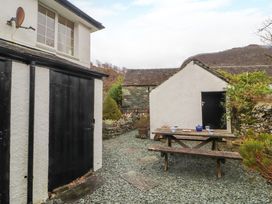 An outdoor area with gravel ground a wooden picnic table with cups and a teapot next to white buildings at Maiden Moor in Grange near Keswick