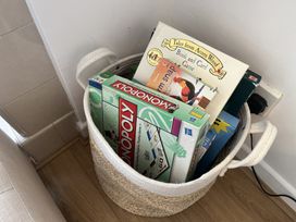 A woven basket containing board games including monopoly and tales from acorn wood in a corner of a room at War Horse Valley Orchard View in Hatherleigh