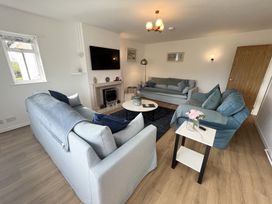 A living room with three sofas a wall-mounted TV and a round coffee table at War Horse Valley Orchard View in Hatherleigh