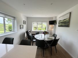 A dining room with a round table set with plates and glasses surrounded by chairs and windows showing greenery at War Horse Valley Orchard View in Hatherleigh