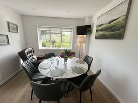 A dining room with a round table set for six people with green chairs and a vase of flowers by a window at War Horse Valley Orchard View in Hatherleigh