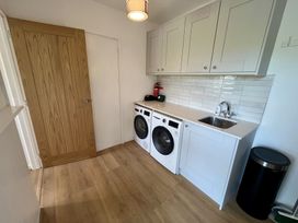 A laundry room with wooden floor two white front-load machines white cabinets a sink and a trash can at War Horse Valley Orchard View in Hatherleigh