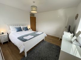 A bedroom with a white bed and two blue pillows a gray rug a white dresser with a mirror a wooden door and a small television at War Horse Valley Orchard View in Hatherleigh