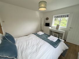 A bedroom with a bed, pillows, a dresser with a small television, a window with a patterned blind, and a desk with a chair at War Horse Valley Orchard View in Hatherleigh