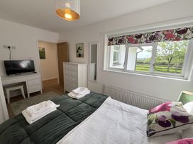 A bedroom with a bed, dresser, desk with a TV, and a window with floral blinds at War Horse Valley Orchard View in Hatherleigh
