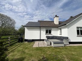 An outdoor patio area with a wicker sectional sofa and ottoman next to a white house at War Horse Valley Orchard View in Hatherleigh
