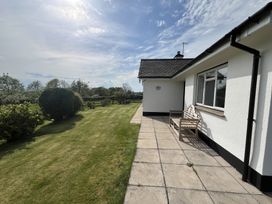 A patio with a wooden bench next to a white house and a lawn with trees at War Horse Valley Orchard View in Hatherleigh