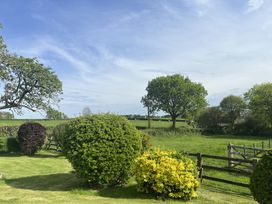 A garden with bushes and trees next to a wooden fence and green fields at War Horse Valley Orchard View in Hatherleigh