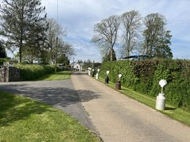 A driveway lined with old milk churns with attached signs beside a hedge and trees at War Horse Valley Orchard View in Hatherleigh