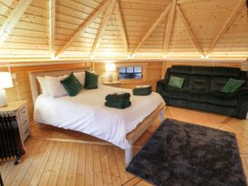 A bedroom with a double bed, green pillows, folded towels, a dark sofa, rug, and wooden walls at The Hideaway in Dungiven Londonderry