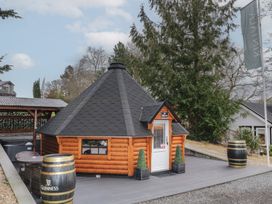 A small wooden cabin with a steep roof and a white door on a deck with barrels and outdoor seating at The Hideaway in Dungiven Londonderry