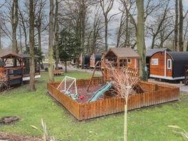 A fenced playground with a slide swing and toy cars surrounded by trees and wooden cabins at The Hideaway in Dungiven Londonderry