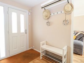 An entryway with a white door a white bench with black metal shoe racks a wall-mounted coat rack with two hats and two heart-shaped decorations a gray sofa visible in the adjacent room at White Lion Retreat in Cromer