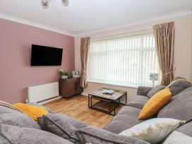 A living room with a grey sofa yellow cushions coffee table and TV on a pink wall at White Lion Retreat in Cromer