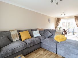 A living room with a gray sectional sofa and cushions next to a dining area with a table and chairs by glass doors at White Lion Retreat in Cromer