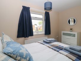 A bedroom with a bed, blue and beige pillows, folded towels, a window with navy curtains, a dresser with a small plant, and a round mirror at White Lion Retreat in Cromer