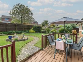 A garden with a paved pathway a circular flower bed and a decked patio with a dining table and chairs under an umbrella at White Lion Retreat in Cromer