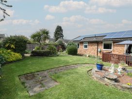 A garden with grass, shrubs, and a small patio next to a brick house with solar panels on the roof at White Lion Retreat in Cromer