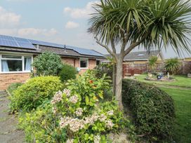 A garden with various plants and a tree in front of a brick house with solar panels on the roof at White Lion Retreat in Cromer