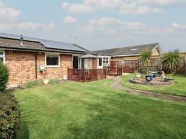 A backyard with green lawn, potted plants, wooden deck with umbrella, and a bench near fences at White Lion Retreat in Cromer