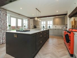 A kitchen with a large island, pendant lights, a red stove, cabinets, and windows near Providence Farmhouse near Easingwold