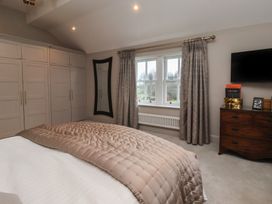 A bedroom with a bed covered with a quilt next to a window with curtains a wooden dresser with books and a television mounted on the wall near fitted wardrobes and a wall mirror at Providence Farmhouse near Easingwold