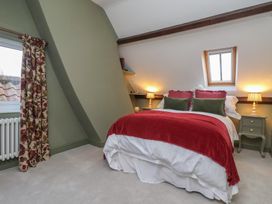 A bedroom with a bed with red and green pillows and a red blanket two bedside tables with lamps a window with floral curtains and a skylight at Providence Farmhouse near Easingwold