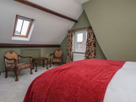 A bedroom with two armchairs a small table and a bed with a red blanket at Providence Farmhouse near Easingwold