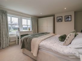A bedroom with a bed green and white bedding a white wardrobe two framed pictures on the wall and a white table under windows with patterned curtains at Providence Farmhouse near Easingwold