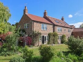 A brick house with multiple windows and chimneys surrounded by a garden with green plants and a metal arch at Providence Farmhouse near Easingwold