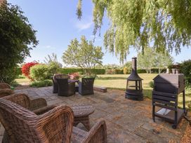 An outdoor patio with wicker chairs a fire pit and a grill overlooking a garden with trees and bushes at Providence Farmhouse near Easingwold