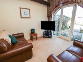 A sitting room with two brown leather sofas a small wooden table and a television by glass doors at Primula Patch in Akeld near Wooler