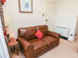 A sitting room with a brown leather sofa and a red cushion next to a wooden side table with a lamp at Primula Patch Akeld near Wooler