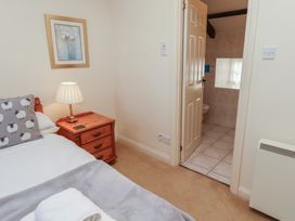 A bedroom with a bed pillow lamp and bedside table with an open door leading to a tiled bathroom at Primula Patch in Akeld near Wooler