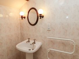 A bathroom corner with a pedestal sink dual taps round mirror and wall lights at Primula Patch in Akeld near Wooler