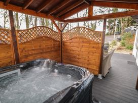 An outdoor hot tub with wooden privacy panels and a covered roof beside a wicker chair on a deck at Drumrane Lodge in Dungiven Londonderry