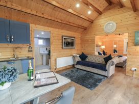 A wooden room with a blue sofa a gray rug blue kitchen cabinets a table with a bottle and flowers and a bed visible in the next room at Drumrane Lodge in Dungiven Londonderry