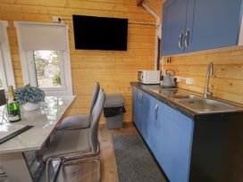A kitchen area with blue cabinets a sink microwave kettle wall mounted tv and dining table with gray chairs at Drumrane Lodge in Dungiven Londonderry