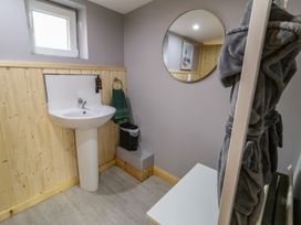 A bathroom with a pedestal sink green towel trash bin round mirror and a gray bathrobe hanging at Drumrane Lodge in Dungiven Londonderry